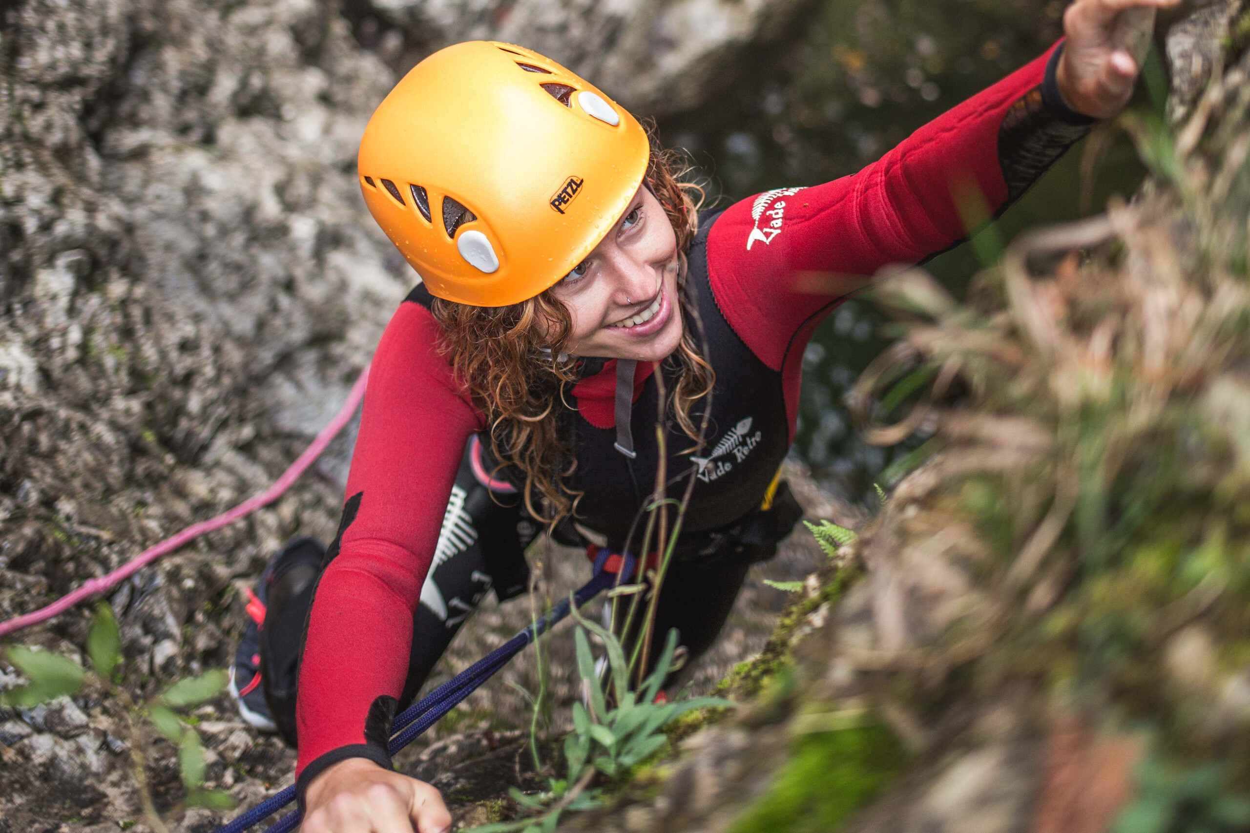 Eine junge Frau klettert beim Canyoning im Salzkammergut die Felswand hoch