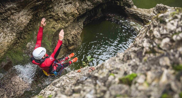 Ein Mann rutscht beim Canyoning in Salzburg auf den nassen Steinen ins Wasser